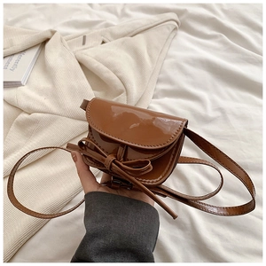 Close-up of brown patent leather mini bag with decorative bow and slim shoulder strap