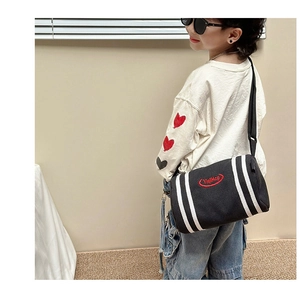 Close-up of children black canvas cylinder crossbody bag with white stripes and red logo