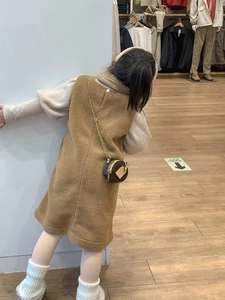 Detail view of a brown plush crossbody round bag with a bronze metal chain on a child outfit