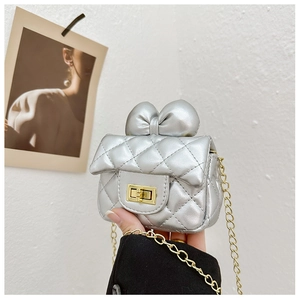 Detailed macro view of silver quilted crossbody bag with bow decoration and gold chain strap