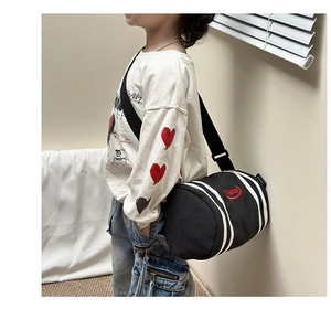 Detail view of black kids cylindrical crossbody bag with white stripes and red logo
