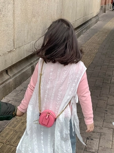 Girl wearing a pink round mini crossbody bag with a gold chain strap and lace vest