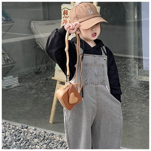Detail of a brown heart-shaped leather crossbody bag worn by a young child model