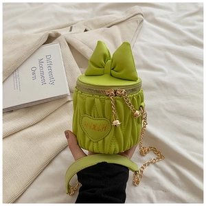 Détail du sac seau vert avec grand nœud, écusson cœur et bandoulière chaîne dorée