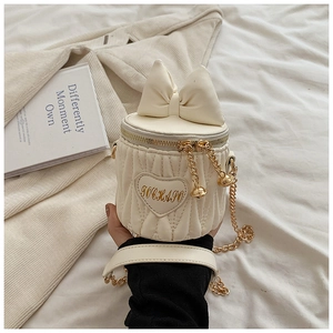 Détail du sac seau blanc avec nœud décoratif, patch cœur et bandoulière en chaîne dorée