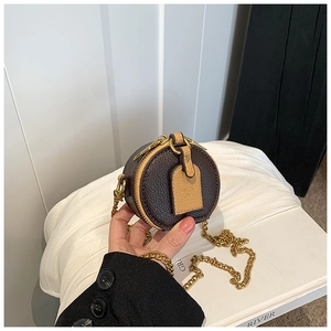 Detail of round mini leather bag showing bronze chain and textured dark brown leather