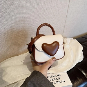 Detail of a mini heart-shaped crossbody bag with contrast handles and adjustable strap