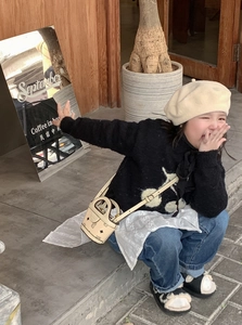Detailed view of child fashion outfit featuring cherry knitwear and khaki mini crossbody bag