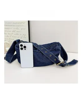 Macro view of blue denim crossbody bag with metal eyelets showing phone size comparison
