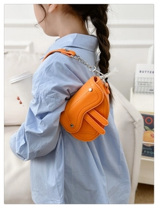 Détail d'un sac selle en cuir orange vif avec bandoulière chaîne porté sur une chemise