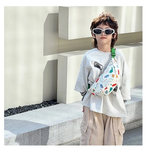 Close-up of child dinosaur print chest bag with green adjustable strap on a young boy