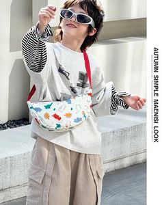 Outdoor shot of a boy wearing a colorful cartoon dinosaur chest bag with a red strap