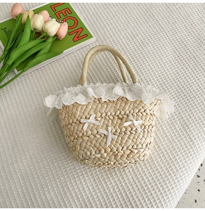 Détail d'un sac seau en paille avec bordure en dentelle blanche et nœuds en satin