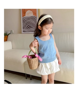 Detail of baby girl summer outfit featuring a light blue knit vest and white bubble skirt
