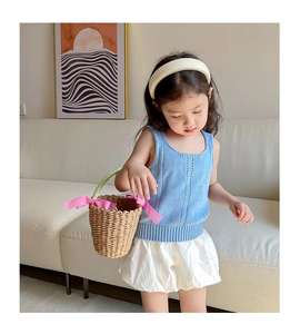 Detail of girls summer outfit with blue knit vest, white shorts and a straw handbag