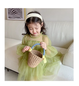 Detail of a girl in a green tulle mesh dress holding a woven straw handbag