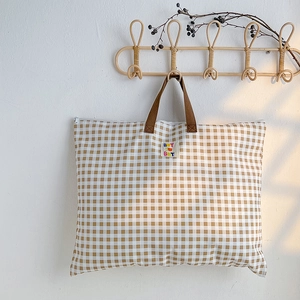 Détail du sac de rangement à carreaux avec poignées brunes et étiquette accrochée au mur