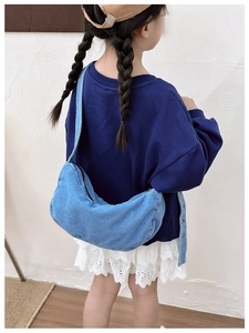 Macro view of washed denim moon bag showing light blue texture and wide strap on child model