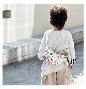 Close-up of a child wearing a white nylon crescent bag with colorful cartoon dinosaurs