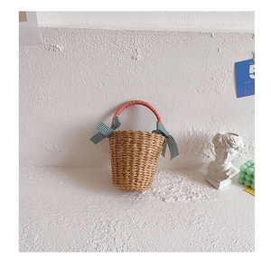 Detail of hand-woven straw beach bag featuring red-white handle and green plaid bows