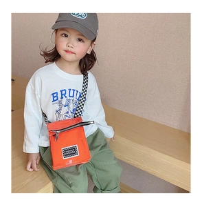 Détail du sac enfant orange avec bandoulière en damier noir et blanc et étiquette
