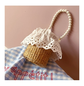 Detail of straw woven bucket bag featuring elegant pearl handle and lace trim on picnic cloth