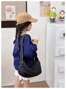 Detail of a grey denim kids crossbody bag showing washed texture and crescent silhouette