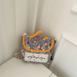 Detail of floral canvas crossbody bag with orange trim and adjustable white shoulder strap
