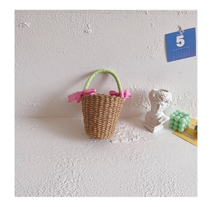Detail of straw hand-woven kids beach bag with green handles and pink plaid bows
