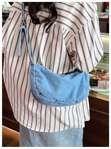 Close-up of light blue denim crescent tote bag with adjustable wide shoulder strap detail