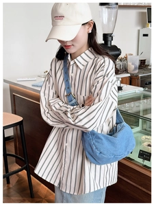 Detail of a light blue denim crescent shoulder bag styled with a striped shirt and cap