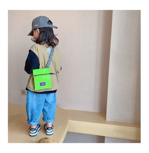 Détail d'un enfant portant un sac bandoulière en cuir verni vert vif avec sangle à damier
