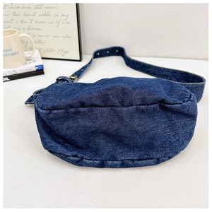 Detailed close-up of dark blue denim crescent bag with adjustable strap and vintage buckle