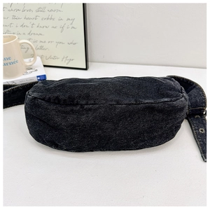 Detail view of the curved bottom and stitched seams of a black denim crescent tote bag