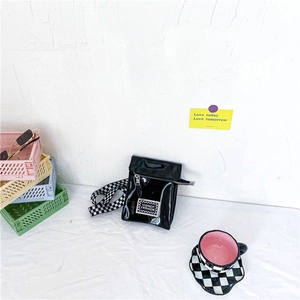 Détail d'un sac bandoulière enfant en cuir verni noir avec sangle à damier et étiquette