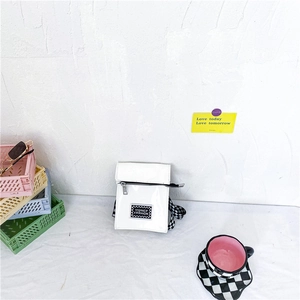 Détail du sac bandoulière enfant en cuir verni blanc avec sangle à damier sur un bureau