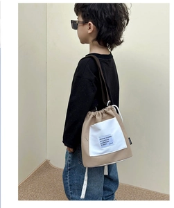 Side view of a khaki and white canvas drawstring bucket bag worn by a child