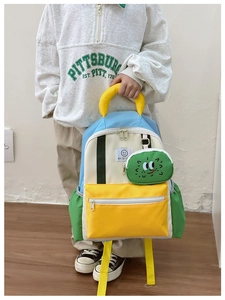 Detail of colorful patchwork kids backpack with yellow pocket and cartoon charm pendant