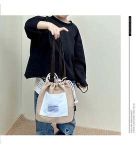 Detail of khaki canvas drawstring bucket bag with white patch pocket and brown handles
