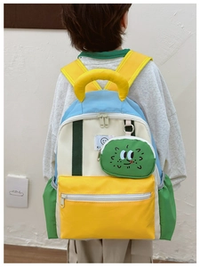 Close-up of color-block kids backpack featuring a green plush monster pendant and durable nylon