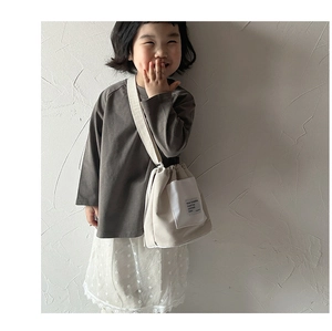Toddler wearing a beige canvas bucket crossbody bag featuring a woven label on the pocket