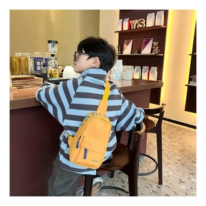 Detail of yellow kids chest bag with blue FASHION text and adjustable strap in cafe