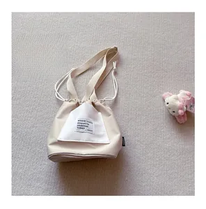 Detail of cream canvas crossbody bag with drawstring closure and black slogan print