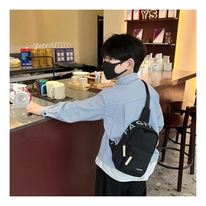 Detail of black nylon kids chest bag featuring white FASHION lettering and zipper pocket