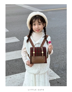 Detail of vintage plaid kids backpack featuring brown leather accents and metal buckles