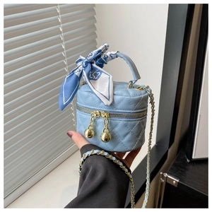 Détail d'un sac cylindre matelassé bleu clair avec anse en soie et bandoulière chaîne