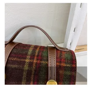 Detailed close-up of red and green plaid wool backpack with brown leather handle and stitching