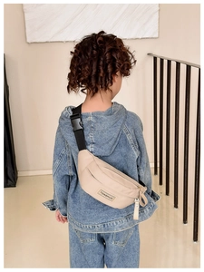 Vue arrière d'un enfant portant un sac bandoulière beige en nylon et sangle noire