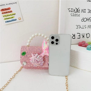 Pink sequin girls mermaid handbag with pearl handle and sea themed charms next to a phone