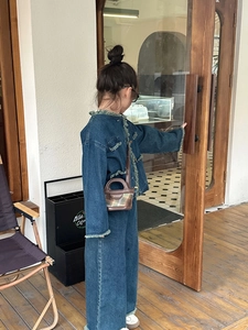 Detail of child wearing denim jacket with fringe edges and brown plaid handbag
